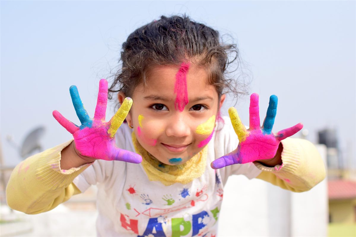 Niña sonriente mostrando las manos cubiertas de pintura de colores